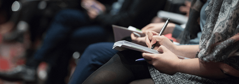 Selective focus photography of people sitting on chairs while writing on notebooks.